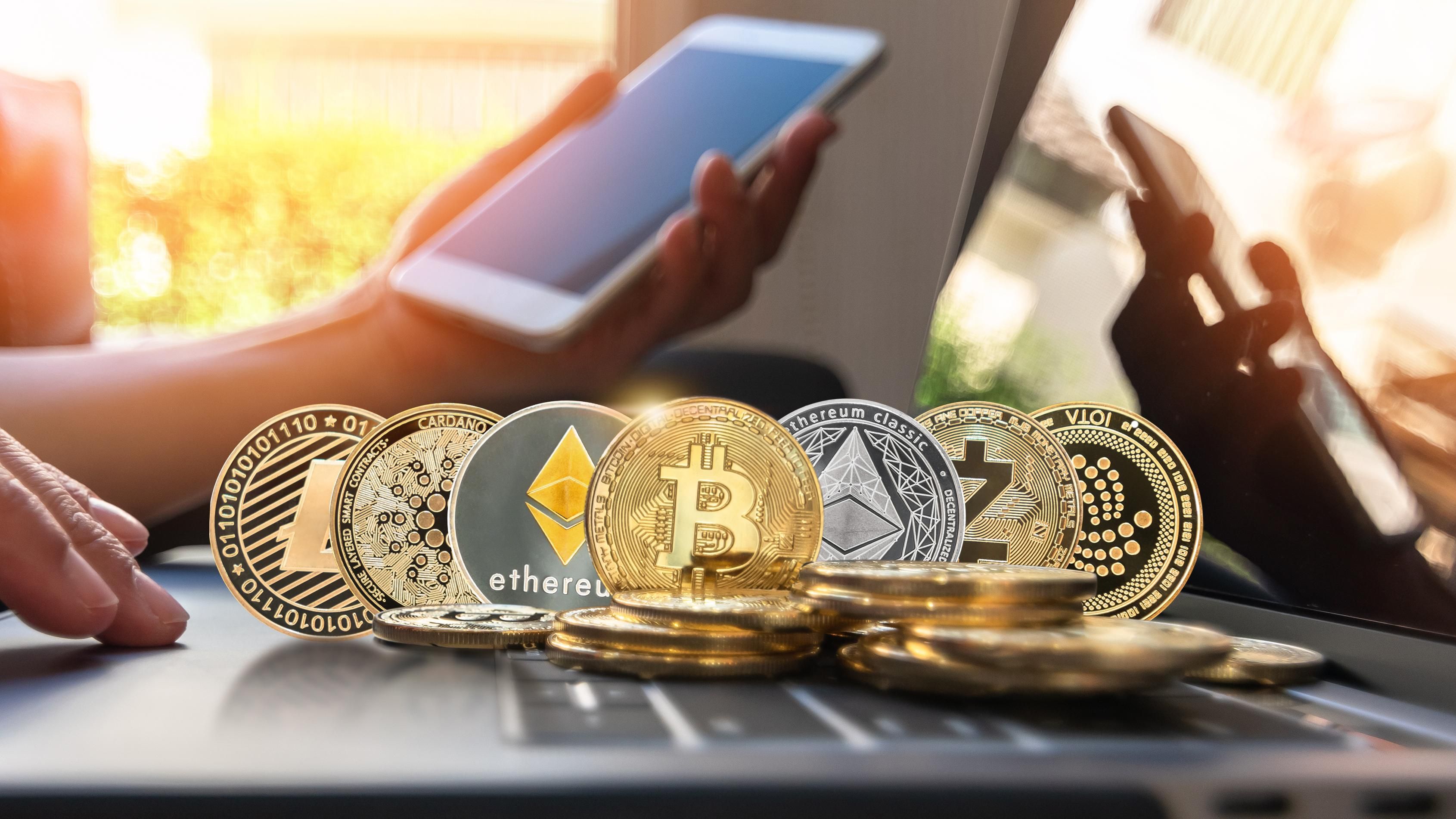 representations of various cryptocurrencies in coin form sitting on a laptop