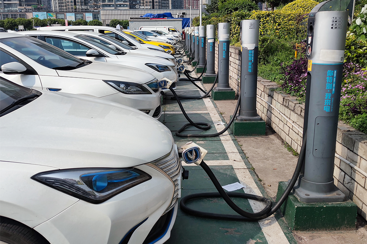 row of electric vehicles in a parking lot plugged into charging stations